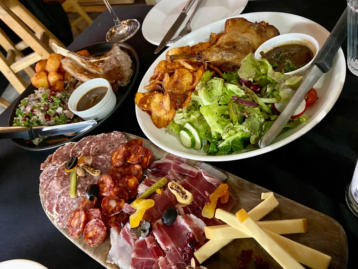 A charcuterie board, duck confit and lamb on a black tablecloth